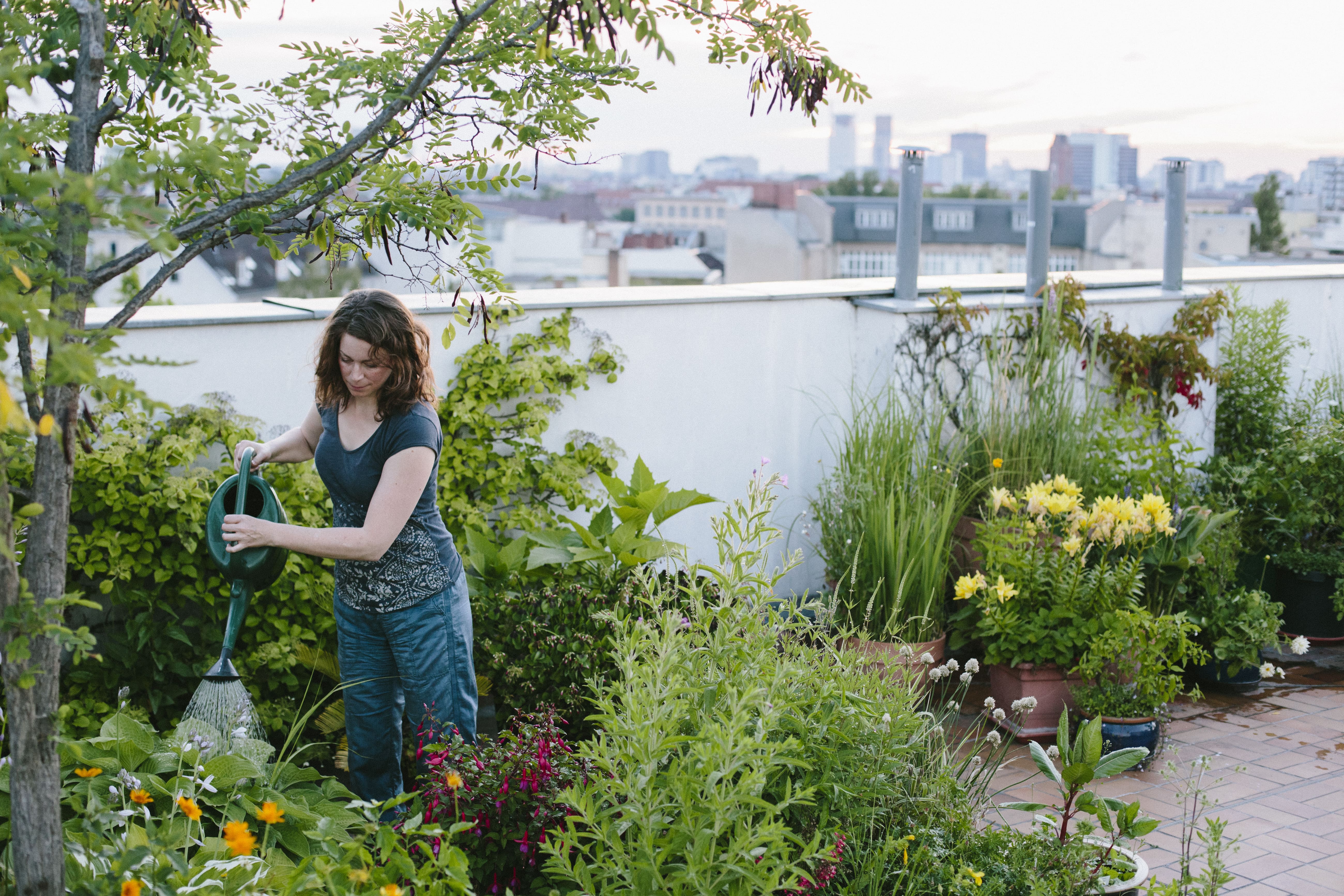 A woman tending to her urban rooftop garden with a city skyline in the background.
